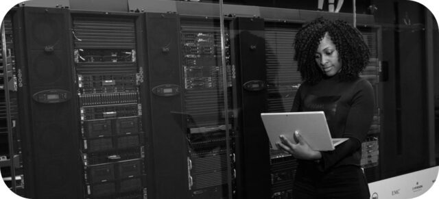 Photographie d'une infrastructure informatique (serveurs). À droite, une femme avec un ordinateur portable.