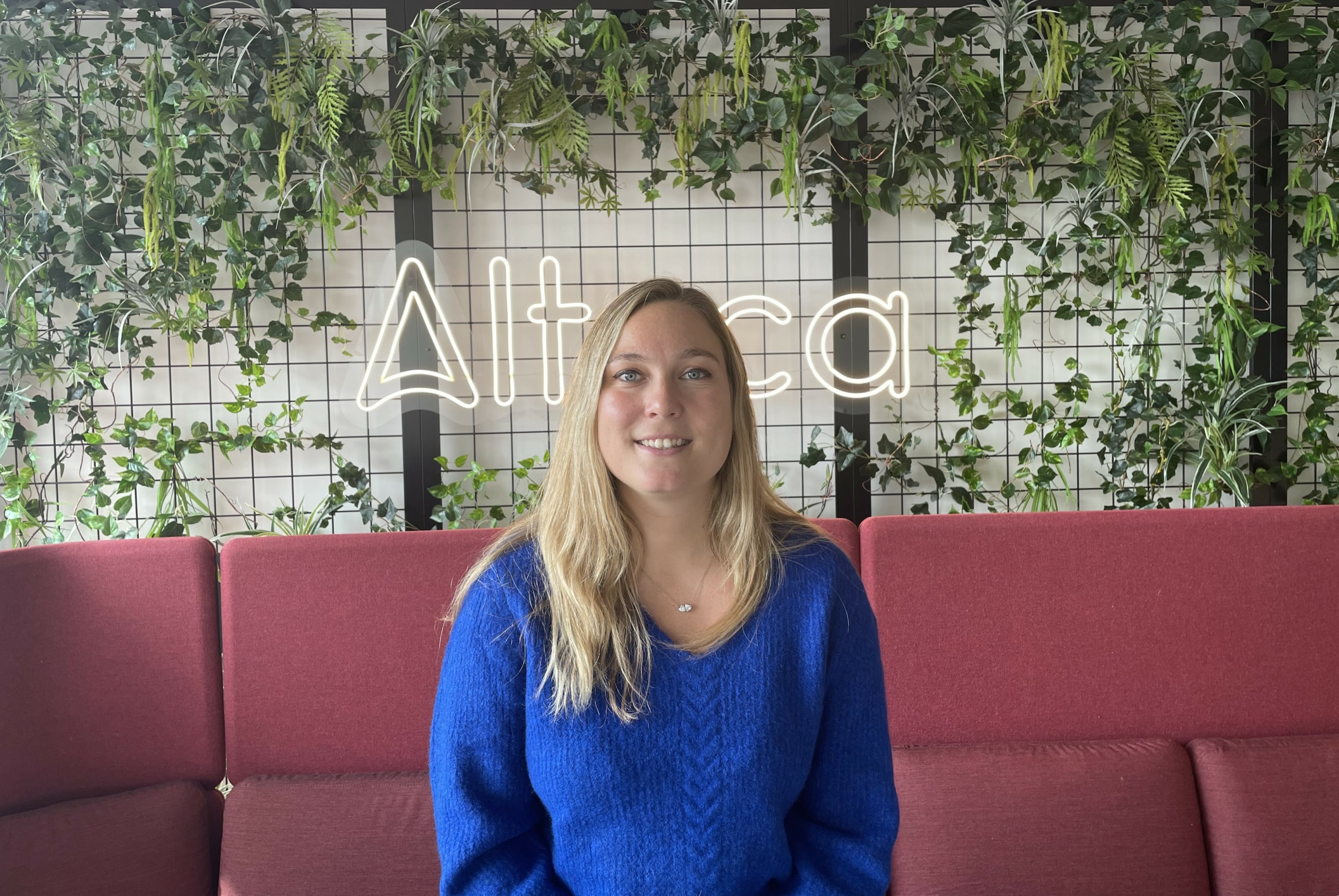 Photo de Fanny, qui exerce le métier de Business Analyst chez Alteca avec un néon Alteca en fond